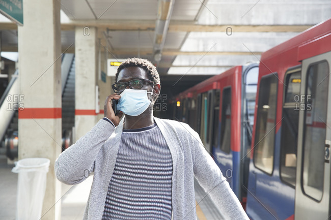 Male entrepreneur wearing protective face mask while talking on mobile phone at railroad station