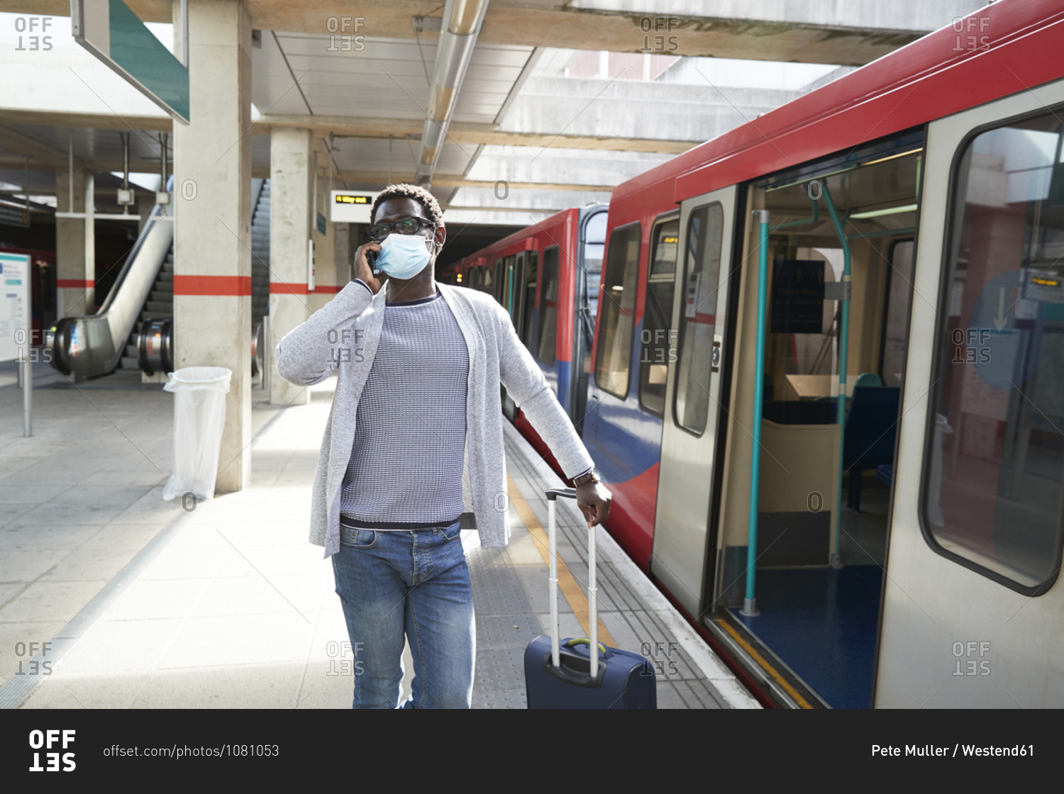 Mature businessman wearing protective face mask talking on phone at railroad station platform