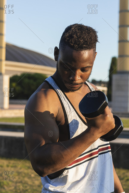Muscular man exercising with dumbbell while standing at park