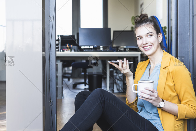 Businesswoman with coffee cup talking on mobile phone while sitting at entrance in office