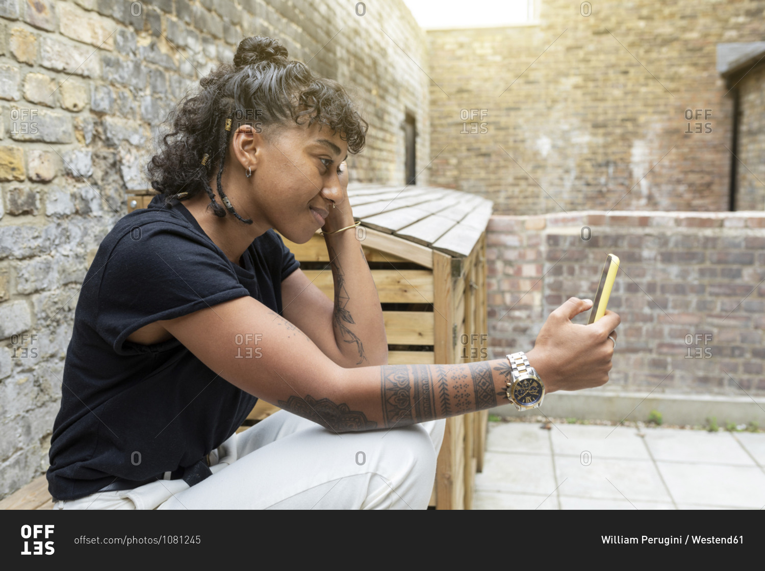 Smiling woman using mobile phone while sitting by wall at back yard