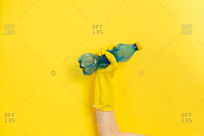 Hand in rubber glove clutches a plastic bottle as a symbol of the struggle for nature. Yellow background