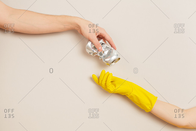 Woman's hand gives garbage to a hand wearing a protective glove on a gray background