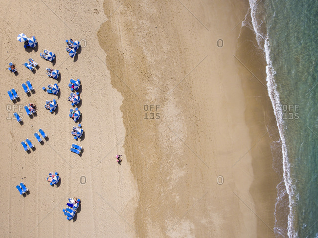 Birds eye view over beach with blue lounge chairs and umbrellas by the ocean