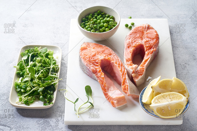 Raw salmon steak top view with micro greens, lemon and green peas. Ingredients for cooking healthy dinner.