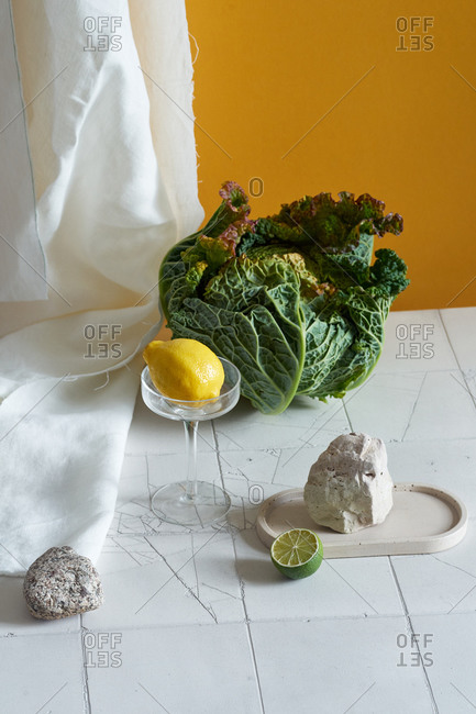 Still life with savoy cabbage, lemon and tiles on yellow background