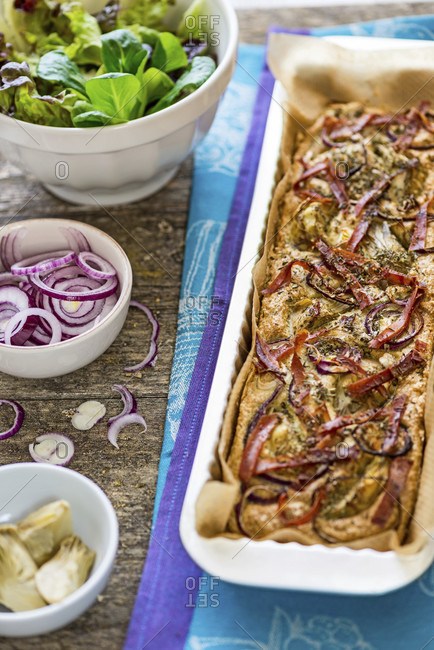 Foccacia fresh from the oven, in a rectangular tart pan, with green salad, extra red onions and artichokes