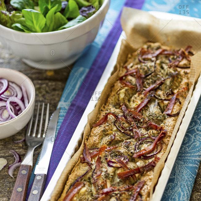 Foccacia fresh from the oven, in a rectangular tart pan, with green salad, extra red onions and artichokes