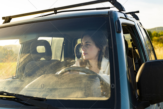 Thoughtful young woman behind windshield looking away while sitting in car during road trip