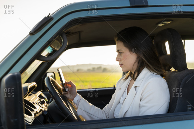 Young woman using mobile phone while sitting in car during road trip