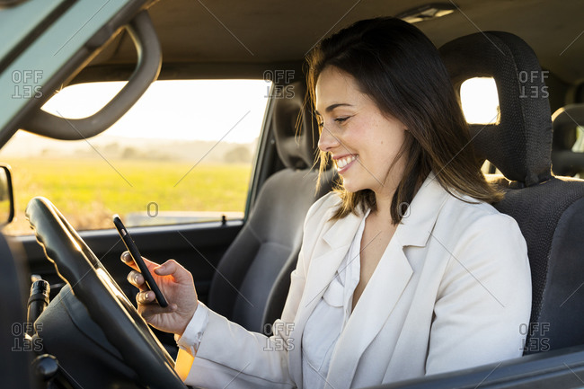 Happy young woman using smart phone in car during road trip