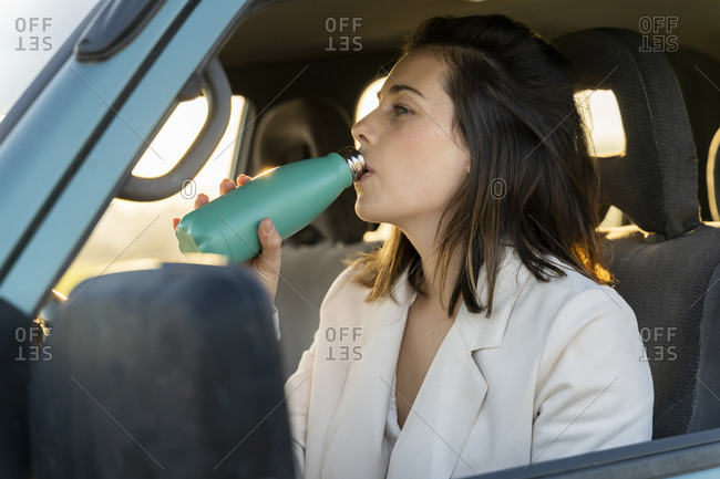 Beautiful young woman drinking water while sitting in car during road trip