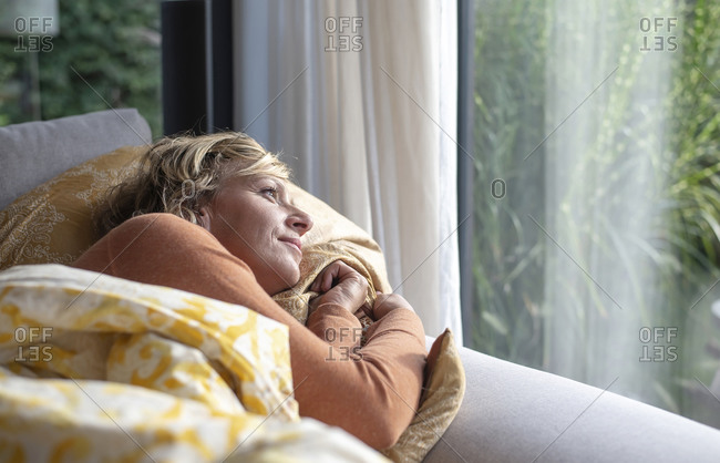 Mature woman looking through window while lying on sofa at home