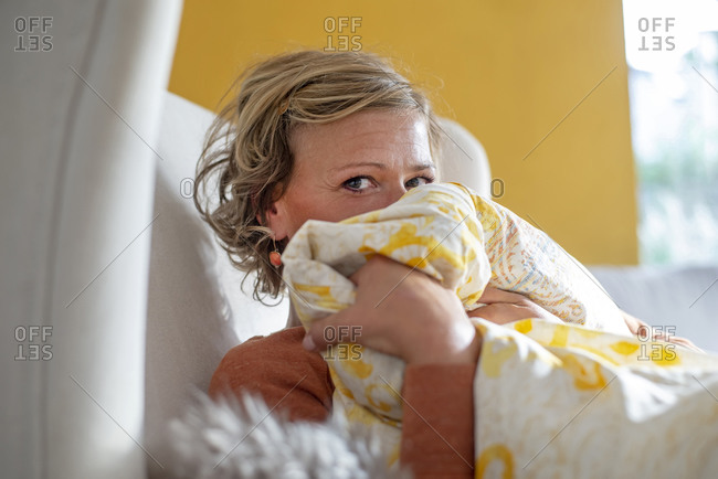 Woman covering face with blanket while sitting on sofa at home