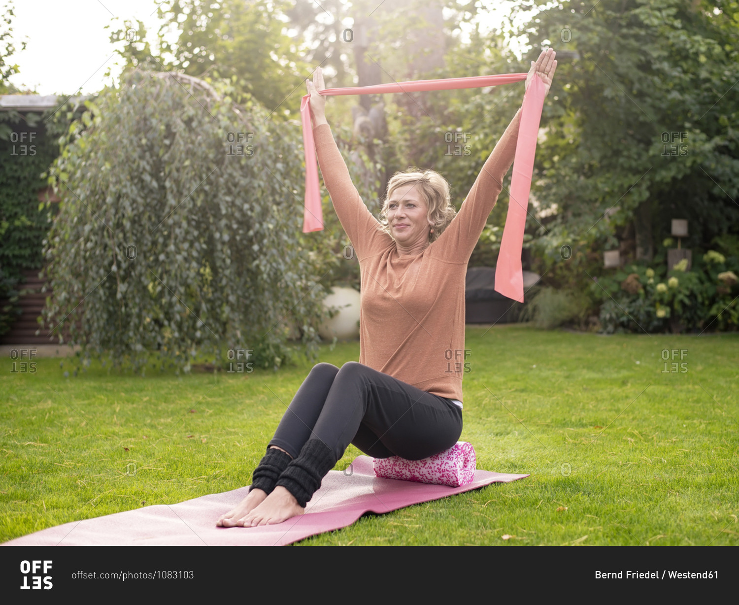 Woman exercising with resistance band while rolling on foam roller at back yard