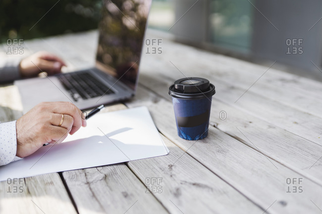 Male entrepreneur with disposable coffee cup working at wooden table
