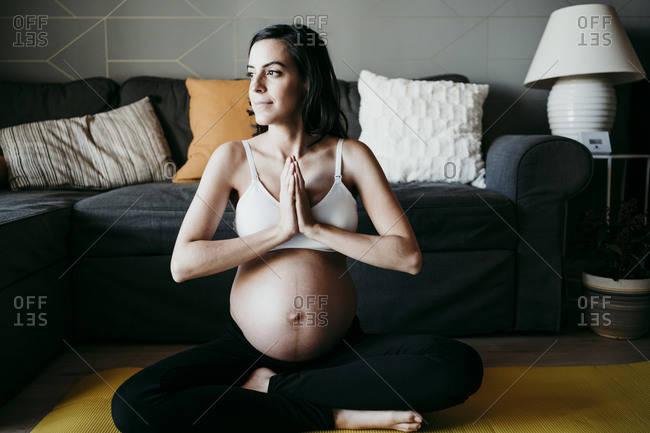 Pregnant woman looking away while exercising in living room at home