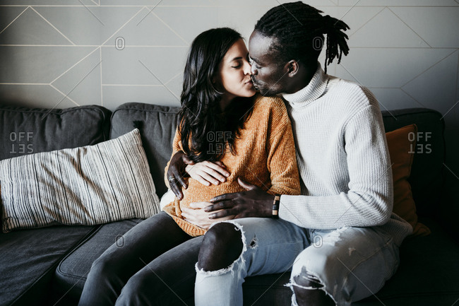 Romantic young man kissing pregnant woman at home