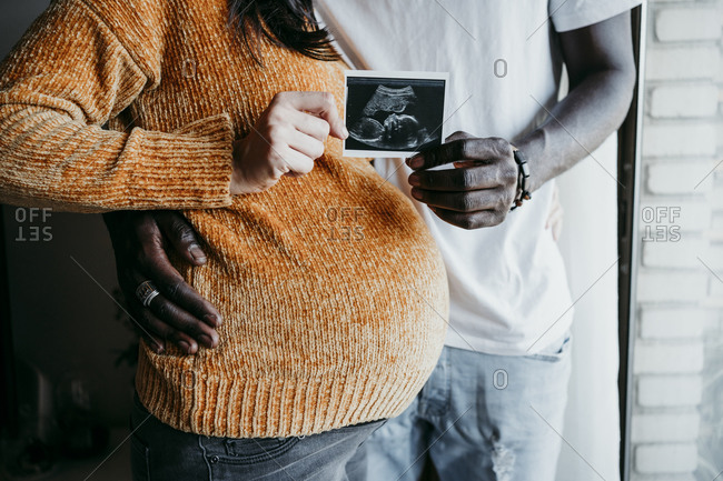Pregnant woman with young man showing ultrasound scan at home
