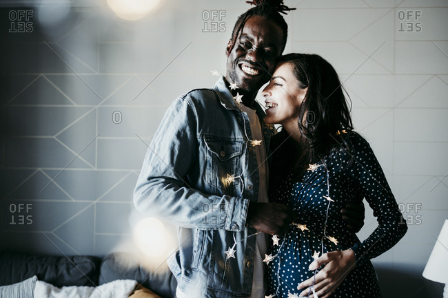 Cheerful young man and pregnant woman with star shaped lights at home