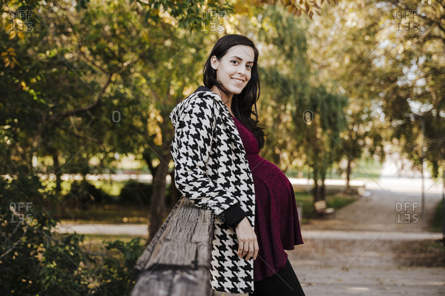 Smiling pregnant woman leaning on wooden structure in park