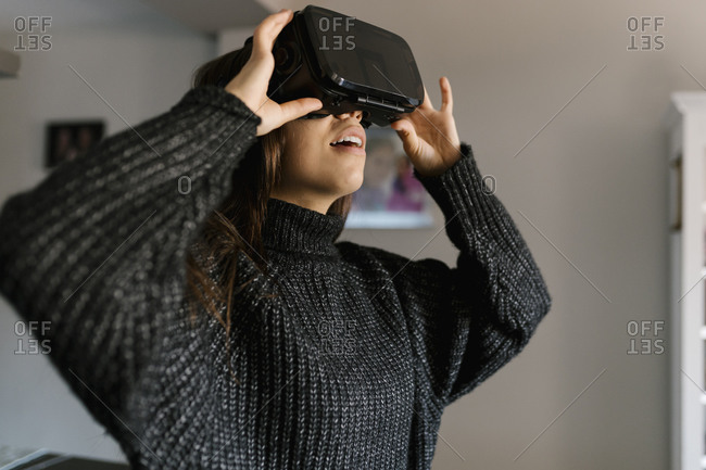 Teenage girl using virtual reality simulator while standing at home