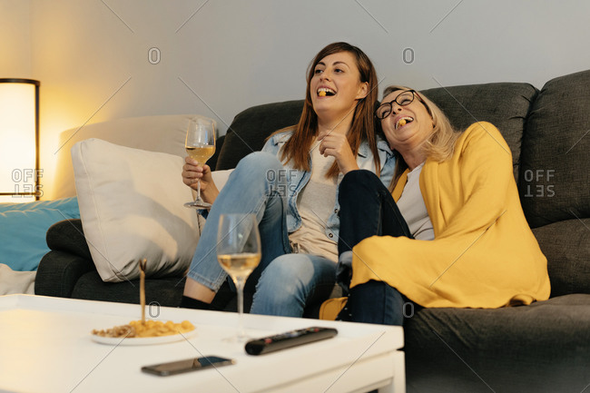 Mother and daughter laughing while eating snacks in living room at home