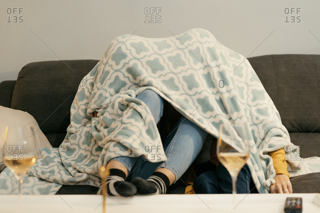 Mother and daughter hiding under blanket on sofa in living room at home