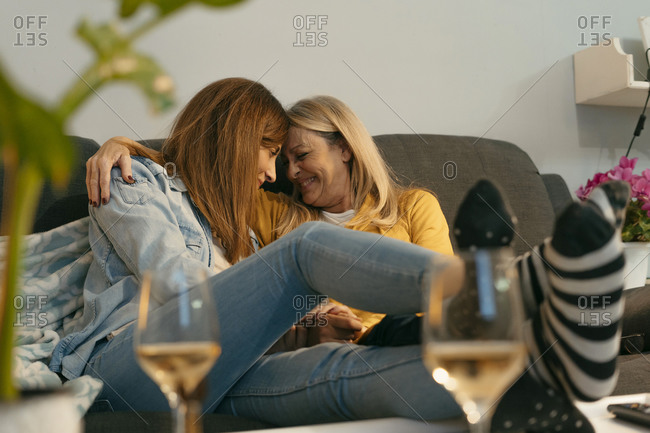 Smiling mother and daughter with arm around touching foreheads on sofa