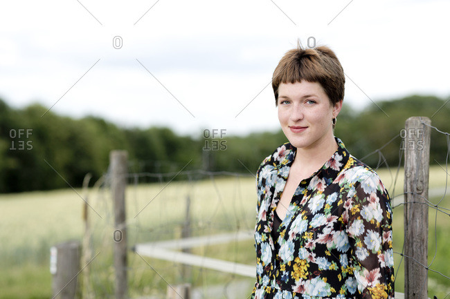 Young woman wearing floral dress standing against fence
