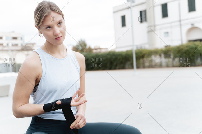 Confident woman looking away while tying boxing wrap in hand outdoors