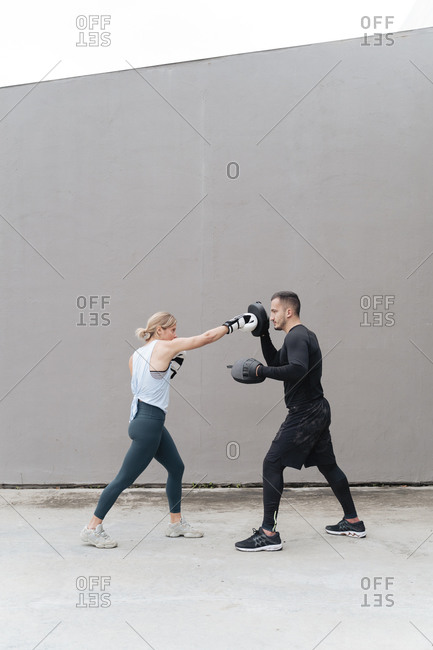 Sportsman teaching boxing to woman while standing against wall