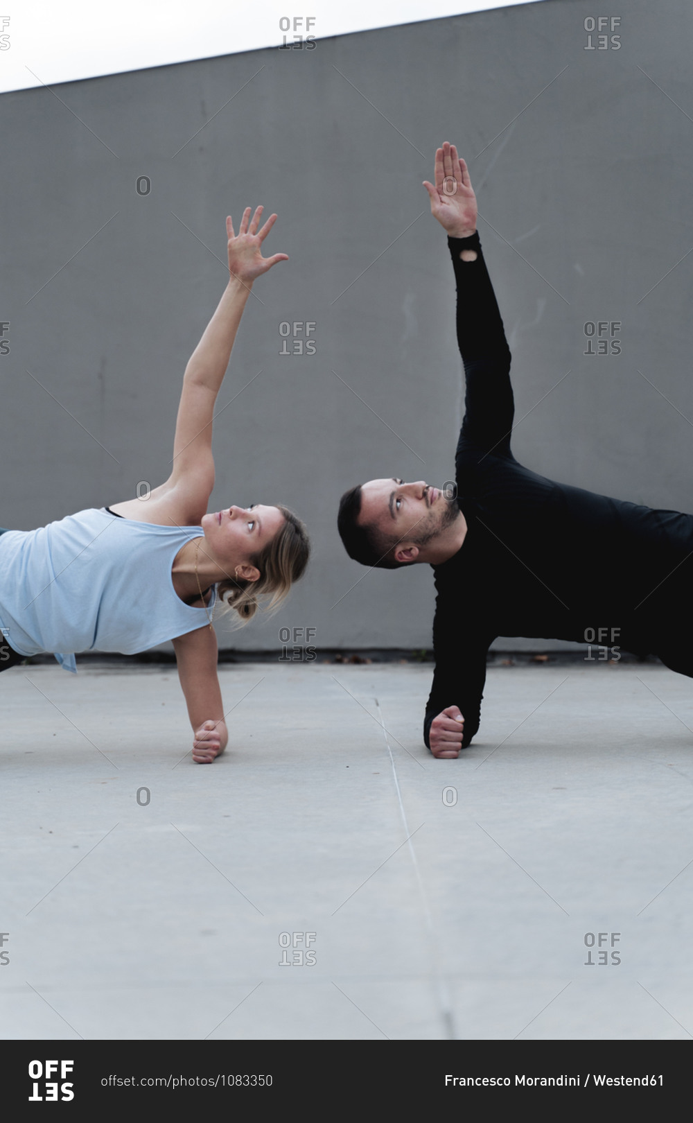 Couple stretching arms while doing side plank pose against wall