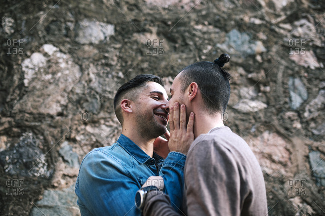 Smiling gay man looking at boyfriend against stone wall