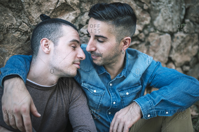Affectionate homosexual men sitting against stone wall