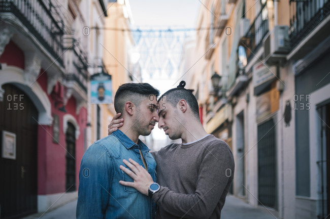Affectionate homosexual men standing against buildings in city
