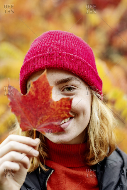 Teenage girl wearing knit hat holding maple leaf outdoor