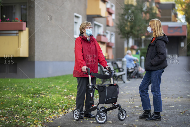 Senior woman with rollator standing by teenage girl in front of retirement home