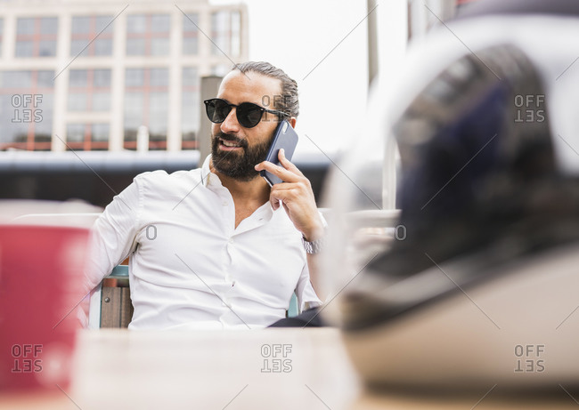 Portrait of bearded businessman wearing sunglasses talking outdoors on smart phone