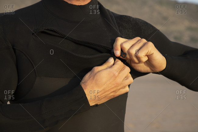 Man zipping black wetsuit at beach