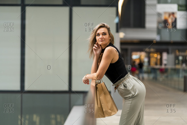 Woman with shopping bags leaning on railing while standing at mall in city