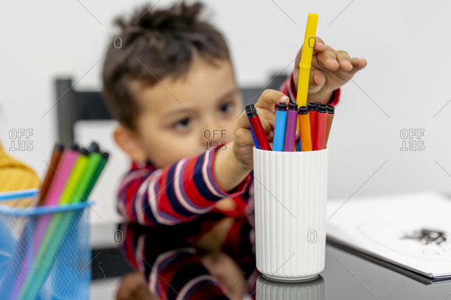 Boy removing sketch pen from desk organizer while learning drawing at home