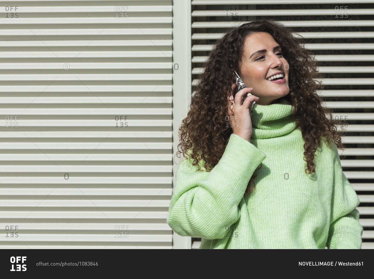 Smiling woman in neon green sweater talking on mobile phone against metallic door
