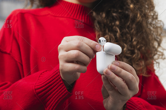 Young woman in red sweater removing wireless in-ear headphones