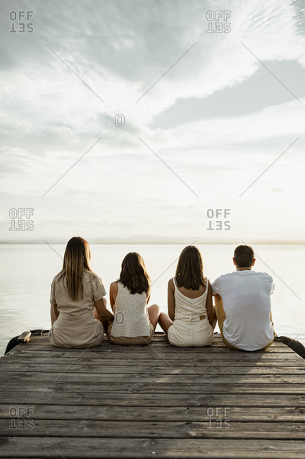 Parents with children looking at lake while sitting at jetty against sky