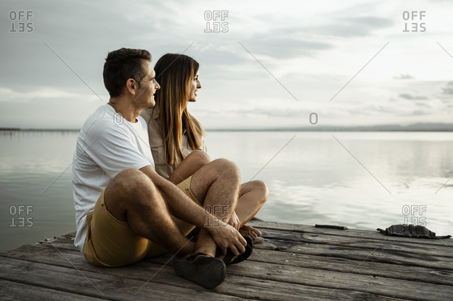 Relaxed mature couple looking away while sitting on jetty against sky