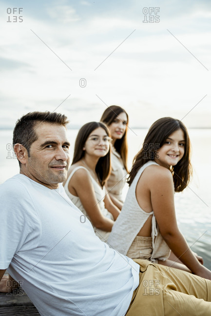 Smiling parents sitting with children at jetty against lake and sky