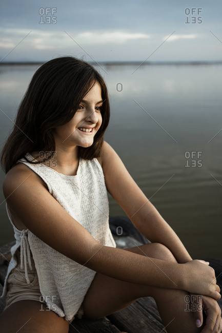 Smiling girl sitting on jetty against lake