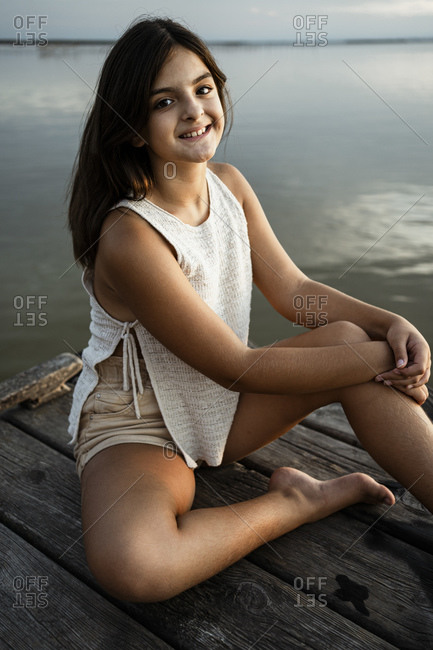 Happy girl sitting on jetty against lake