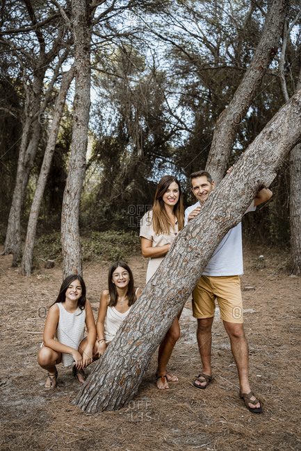 Mother and father with daughters behind tree trunk in forest